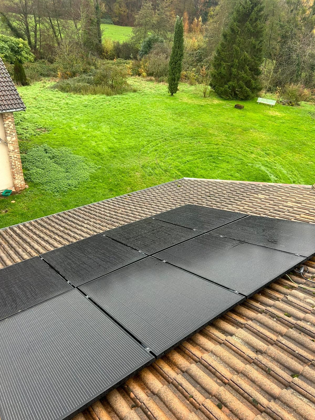 Panneaux photovoltaïques noirs sur un toit en tuiles, avec une pelouse et des arbres en contrebas