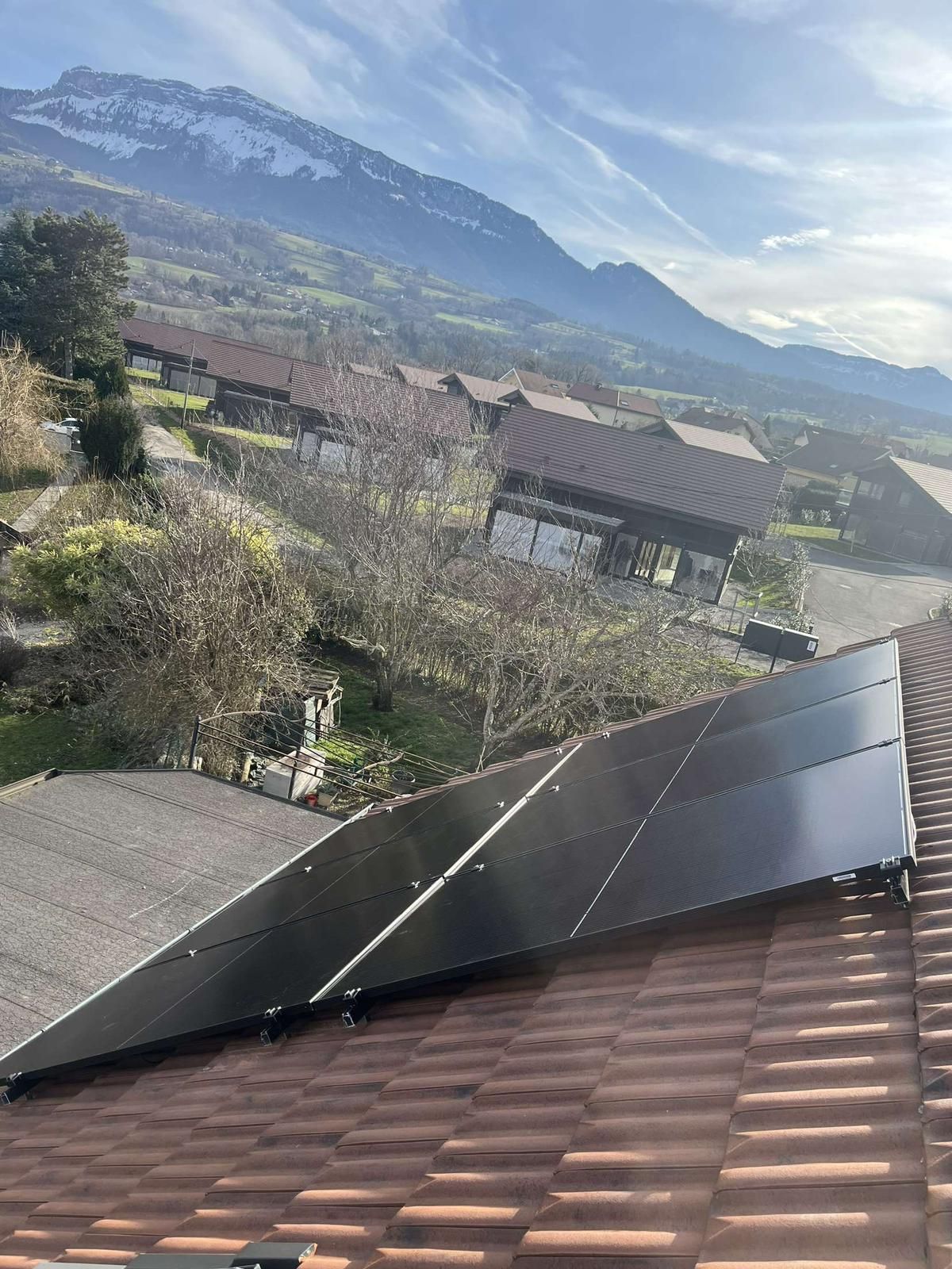 Panneaux photovoltaïques sur un toit en tuiles, avec un village et une montagne enneigée en arrière-plan