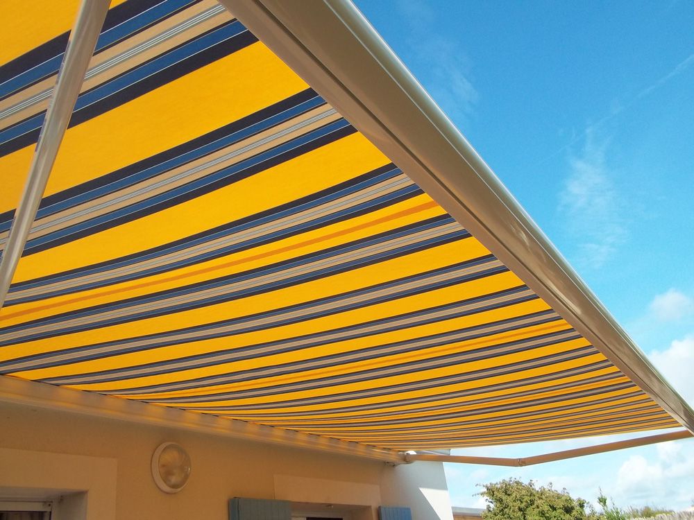 Toile de store banne à rayures jaunes, grises et bleues vue de dessous, sur fond de ciel bleu