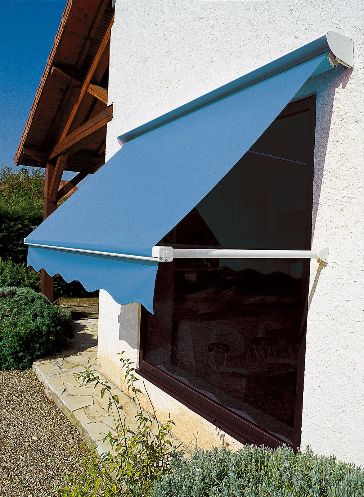 Store à projection à toile bleue protégeant une grande fenêtre sur une façade crépie blanche