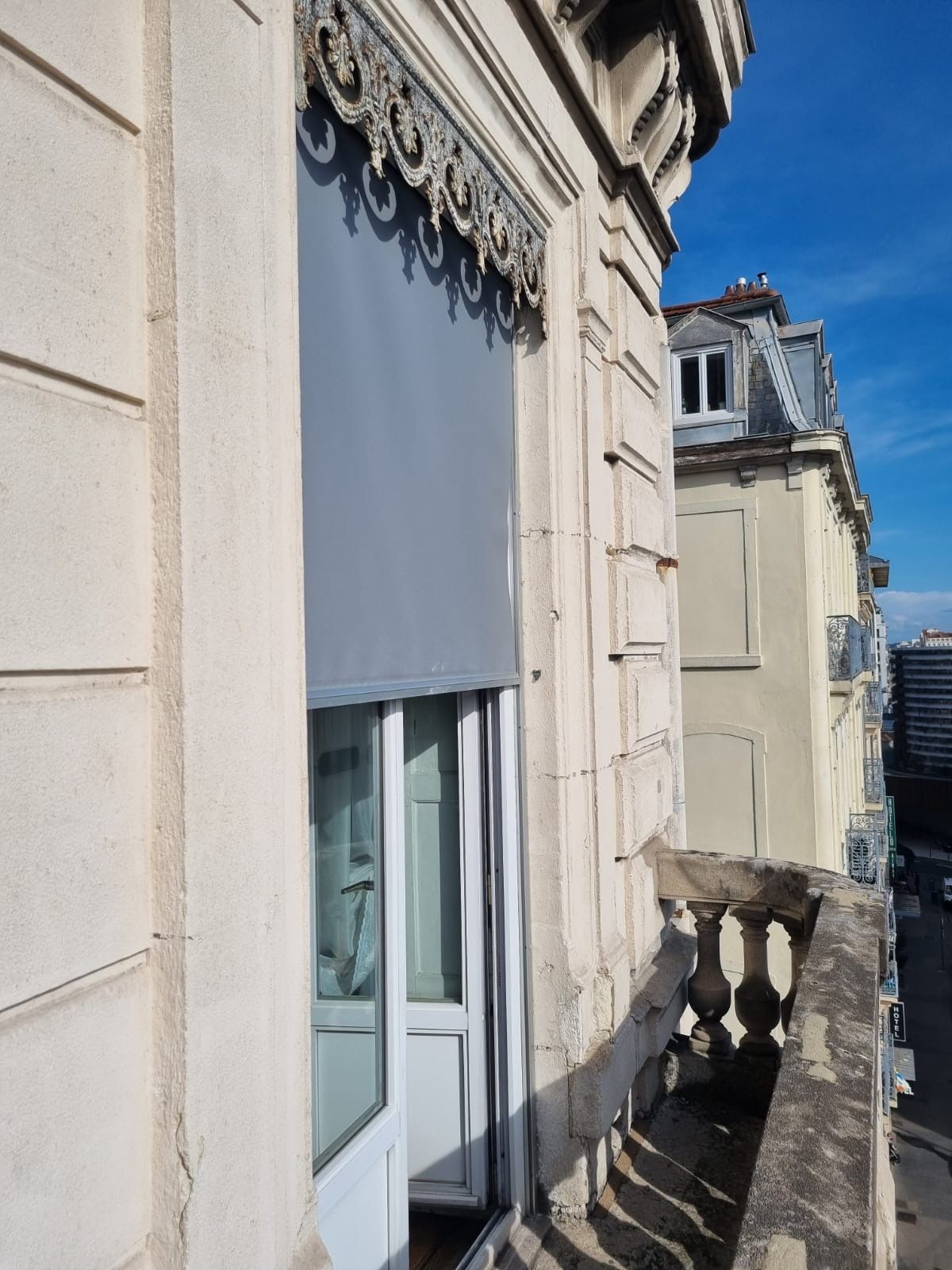 Store vertical gris posé sur une porte-fenêtre d'immeuble ancien à balcon