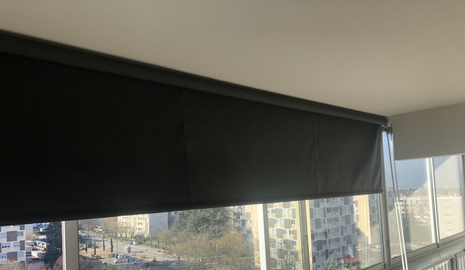 Store enrouleur intérieur gris foncé occupant toute la largeur d'une loggia vitrée