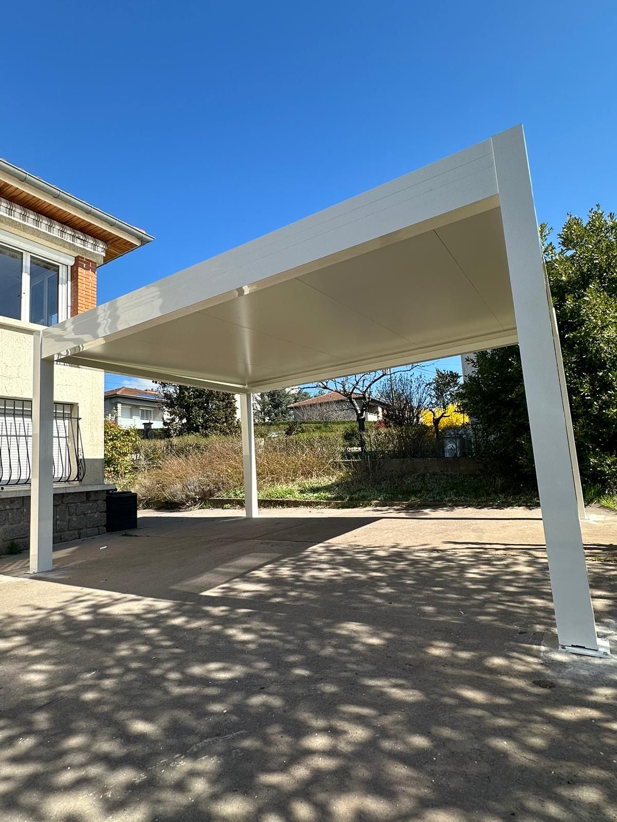 Pergola en aluminium blanc installée au-dessus d'une cour, sous un ciel bleu
