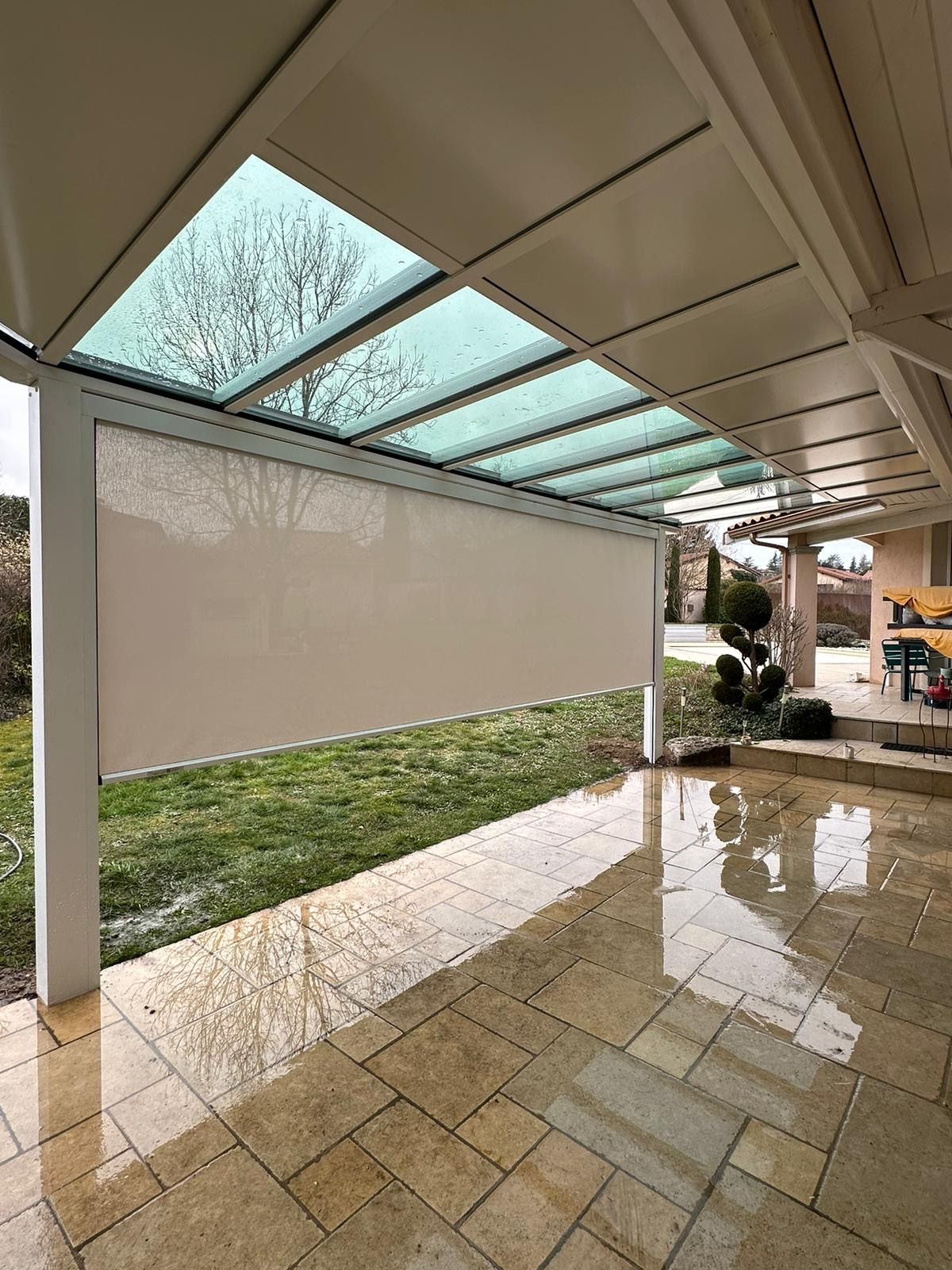 Pergola à toiture partiellement vitrée avec store vertical en toile déroulé, sur une terrasse en pierre