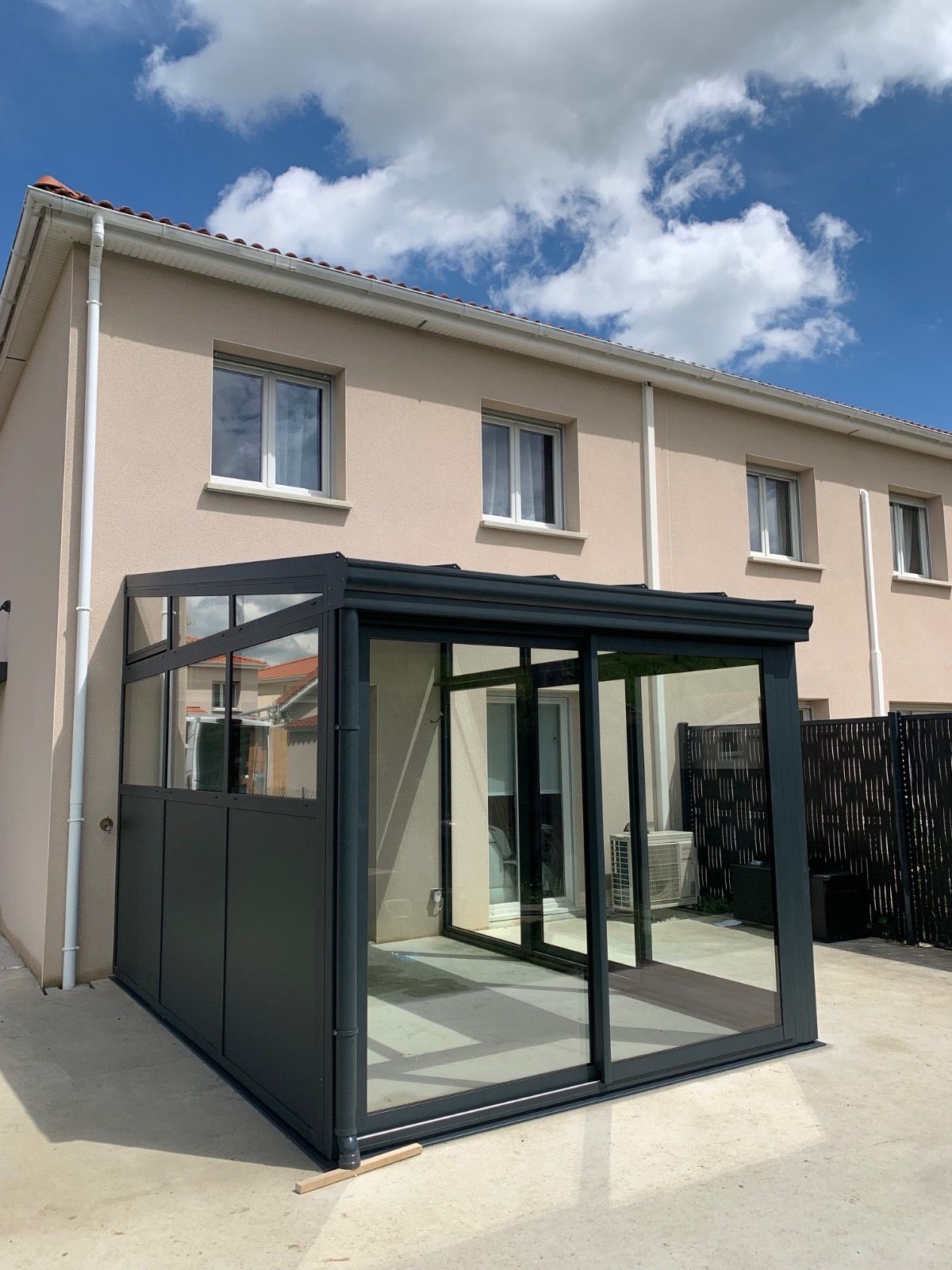 Véranda en aluminium gris anthracite avec baie coulissante, accolée à l'arrière d'une maison
