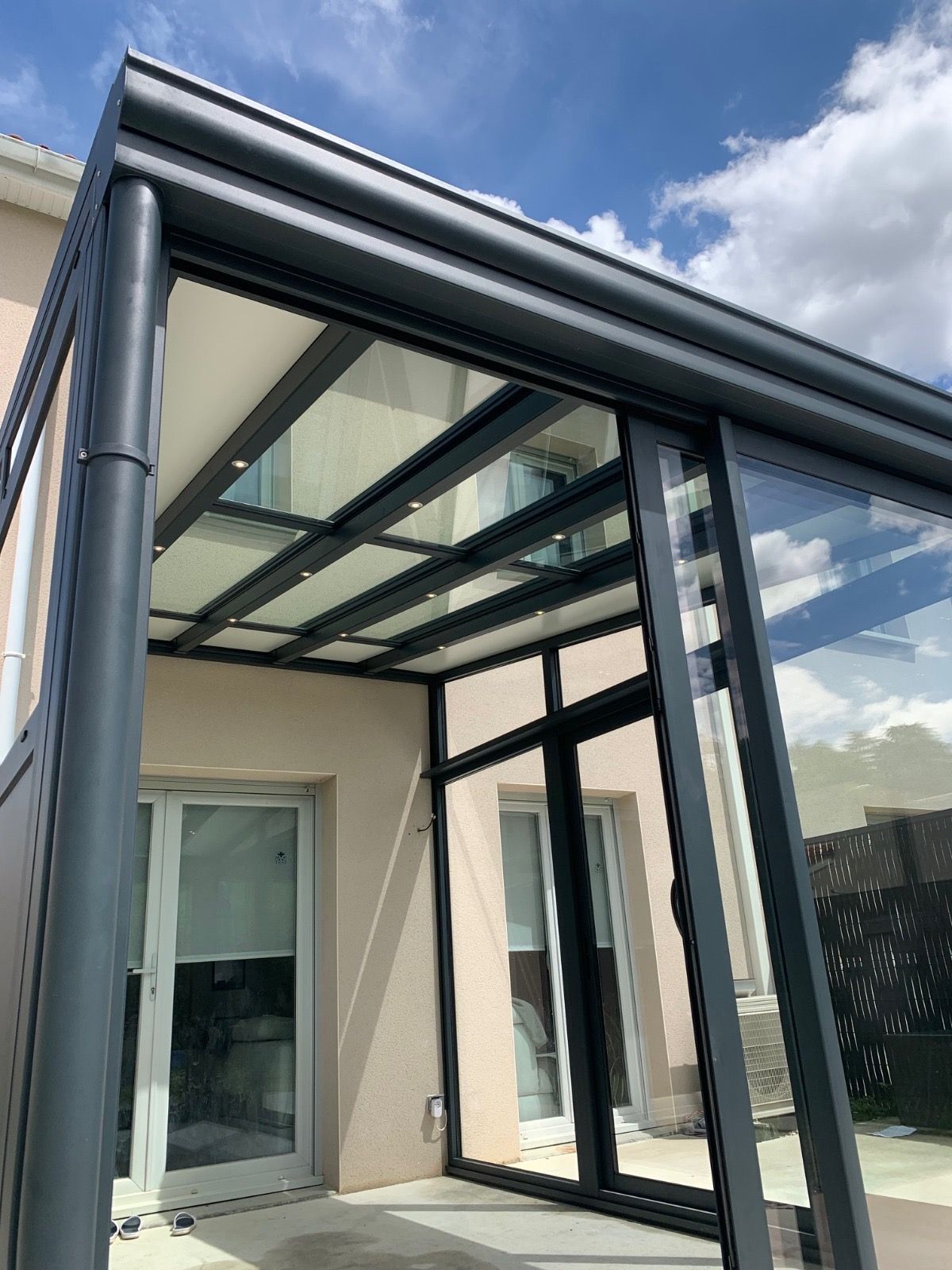 Véranda en aluminium gris avec toiture vitrée et spots intégrés, vue depuis l'extérieur