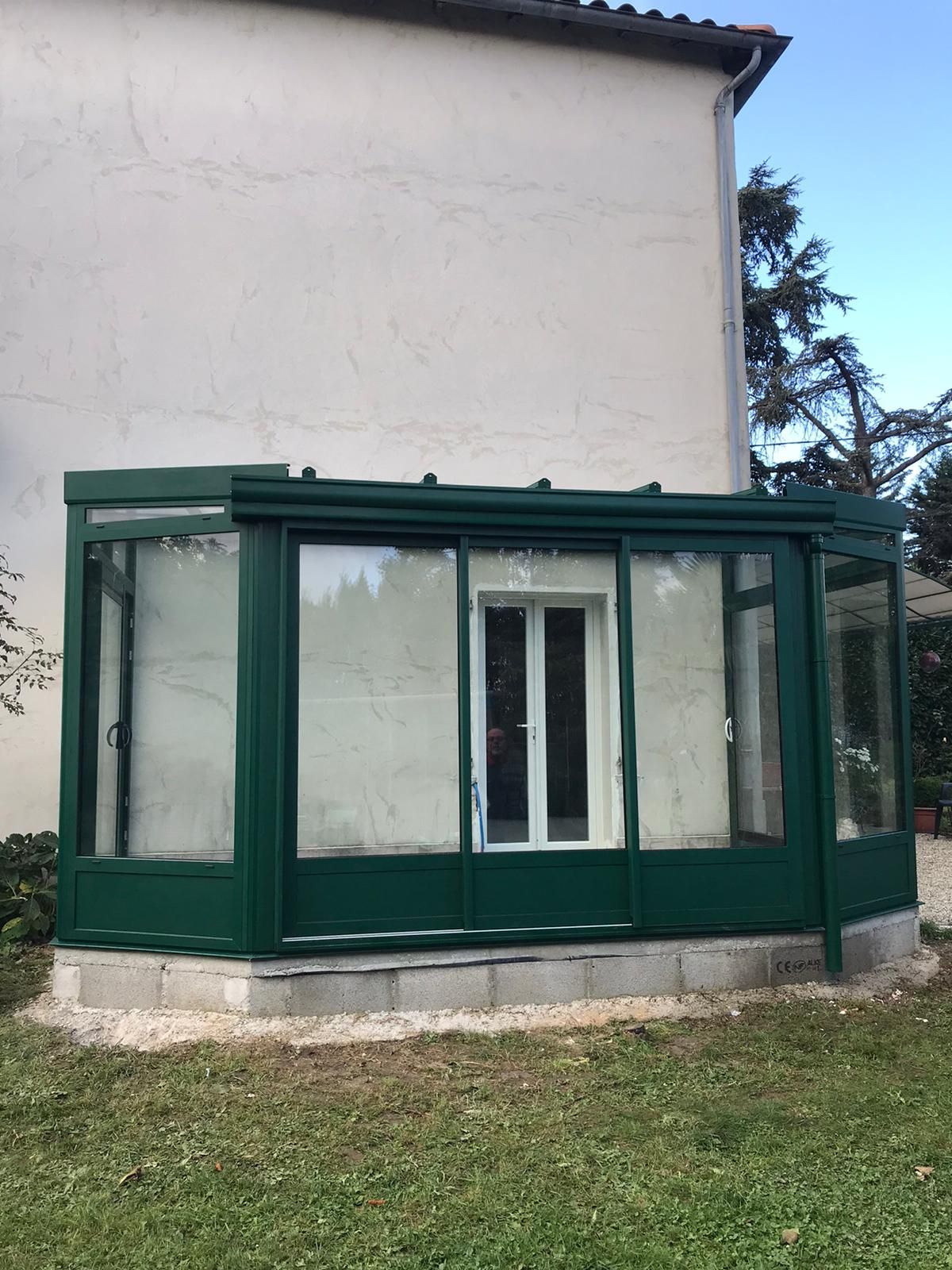 Véranda aux profilés verts adossée à une maison, au bord d'une pelouse