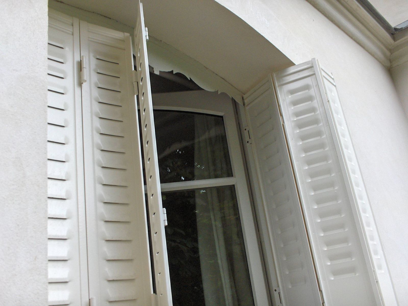 Persiennes blanches à lames ouvertes de part et d'autre d'une porte-fenêtre cintrée
