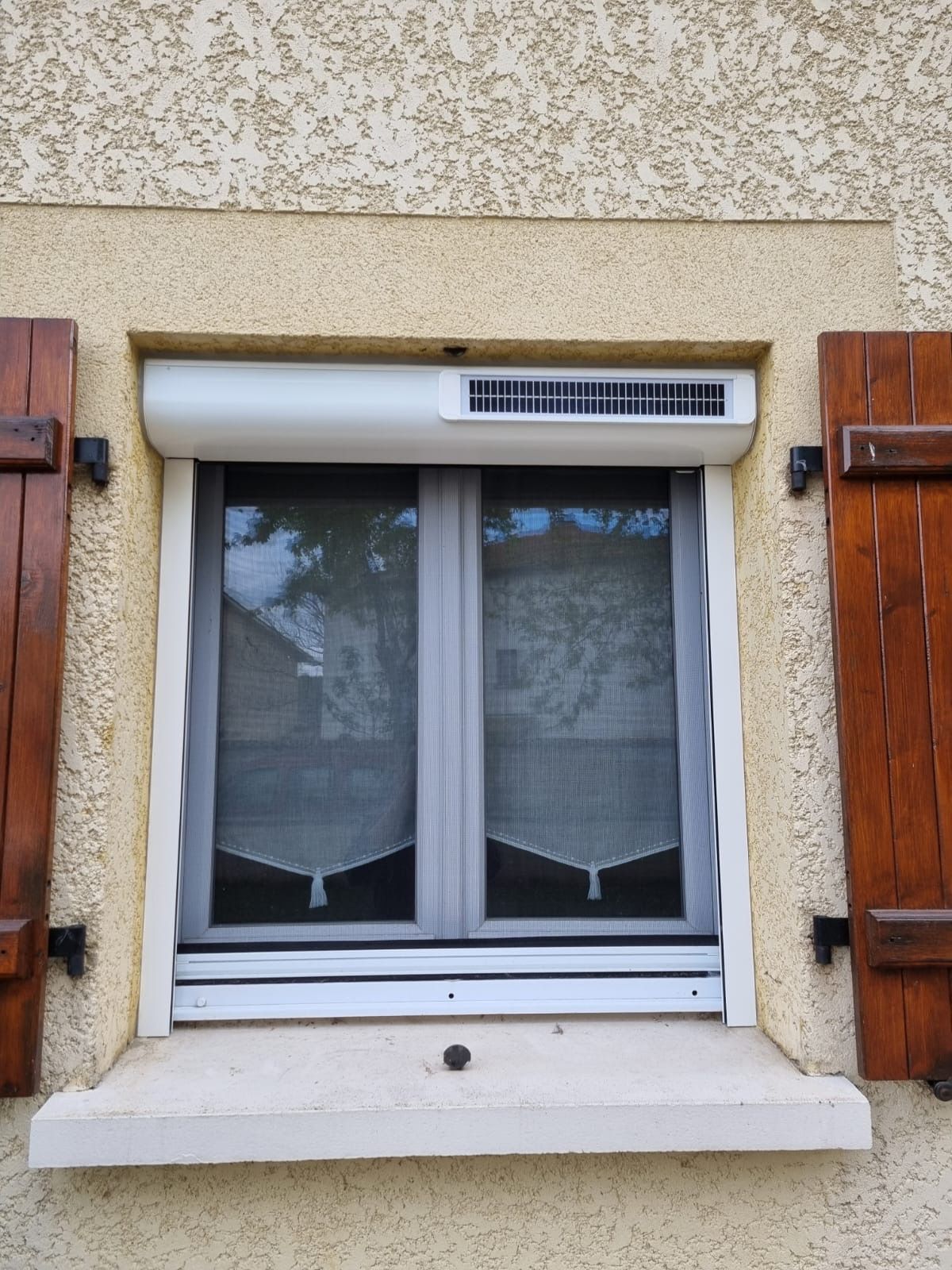 Volet roulant à coffre extérieur avec petit panneau solaire, posé sur une fenêtre blanche