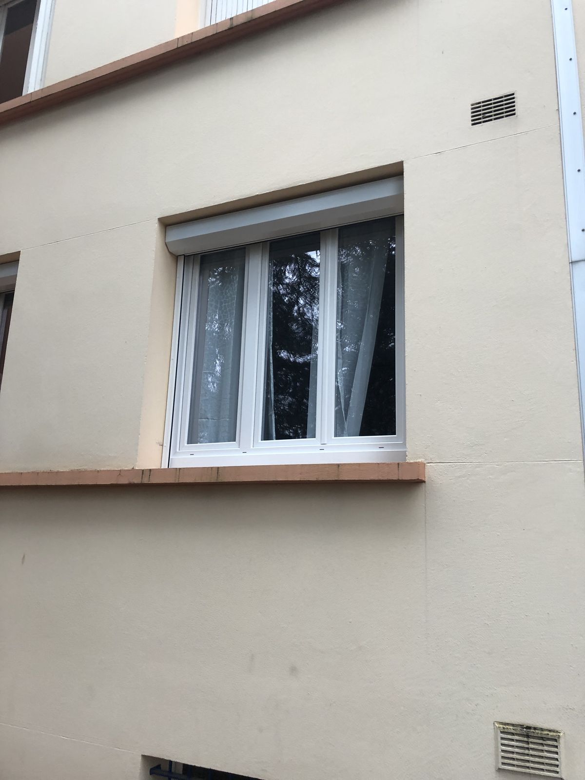 Façade avec une fenêtre PVC blanche à trois vantaux surmontée d'un volet roulant